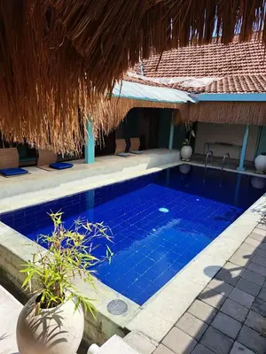 a swimming pool next to a building with a straw roof at Lavender Villa 7 Moon House in Kuta
