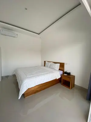 a white bedroom with a bed and a night stand at Hidden Homestay Jimbaran in Jimbaran