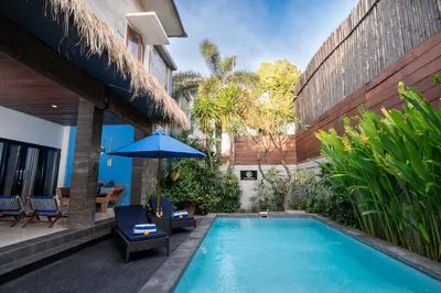 a pool with chairs and an umbrella next to a house at Villa De Ocean in Seminyak
