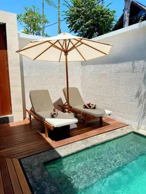 a pair of chairs and an umbrella next to a swimming pool at Villa Alkasa - Legian 400m to beach in Badung