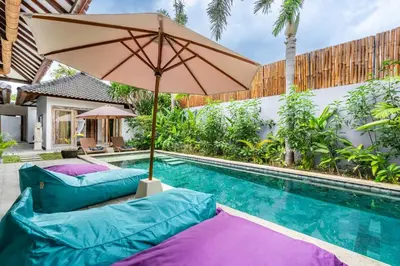 an umbrella sits next to a swimming pool with two pillows at Balima Villa in Seminyak