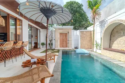 an outdoor patio with a pool and chairs and an umbrella at Villa O'Anne 3 in Seminyak