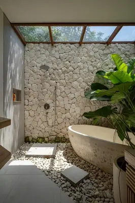 a bathroom with a bath tub and a stone wall at Kona Resort - Seminyak in Kerobokan