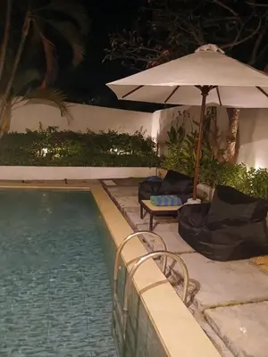a pool with an umbrella and a chair and a table at Villa Private In Kuta Bali in Kuta