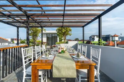 a patio with a wooden table and white chairs at Villa Narda Seminyak by Nagisa Bali in Legian