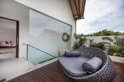a wicker chair sitting on a balcony with a glass wall at Villa K Seminyak by Premier Hospitality Asia in Seminyak