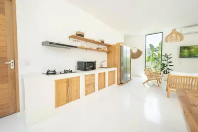 a kitchen with white walls and wooden cabinets at Villa Amie Elegant 5BR with Pool & Rooftop Umalas in Canggu