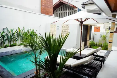 an umbrella and chairs next to a swimming pool at Villa Maharani Sanur in Sanur