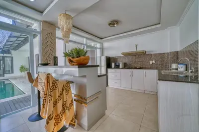 a kitchen with white cabinets and a table and a pool at Rumah Bella Private Villa 3 Bedroom 3 Bathroom in Jimbaran