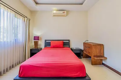 a bedroom with a red bed and a dresser and a window at Panatai Villa in Sanur