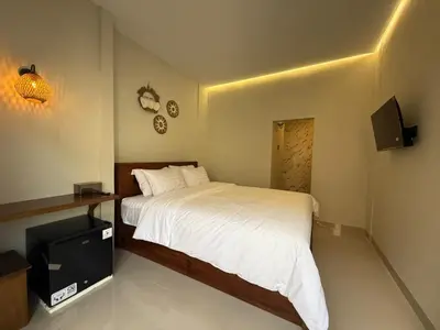 a bedroom with a white bed and a television at Flamboyant Guesthouse in Seminyak