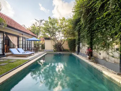 a swimming pool in a yard with two chairs and an umbrella at Villa Cometa Prime Seminyak by Adam Jyota Management in Seminyak