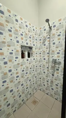 a bathroom with a shower with a tile wall at Banana Room Near to Kuta Legian Beach in Legian