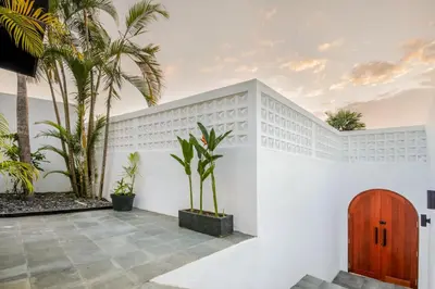 a white house with palm trees and a wooden door at Villa Stella Belle Seminyak in Seminyak