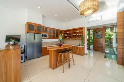 a kitchen with wooden cabinets and a table in it at Lux Ayuni Big Modern 2BR Designer Villa Berawa in Canggu