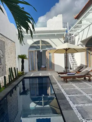 a swimming pool with chairs and an umbrella next to a house at Mediterranean Villa Sanur Beach in Sanur