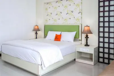 a bedroom with a white bed with an orange pillow at First Home Stay in Ngurah Rai International Airport