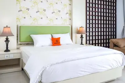 a bedroom with a large white bed with an orange pillow at First Home Stay in Ngurah Rai International Airport
