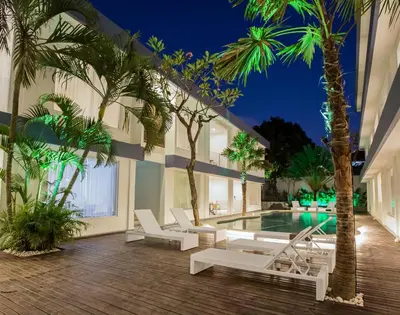 a hotel with a pool with palm trees and lounge chairs at Coast Boutique Hotel in Kuta
