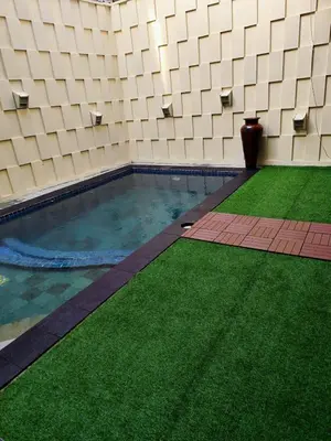a swimming pool with green grass next to a building at The Fatul Villa in Ngurah Rai International Airport