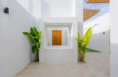 a white hallway with a door and two plants at Villa Bellora by Pertama Management in Seminyak