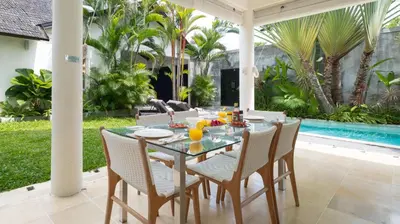 a dining table and chairs on a patio with a pool at Villa Merta Sari 8 by Villa Finder in Seminyak