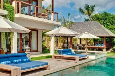 a villa with a swimming pool with blue chairs and umbrellas at Calista Peaceful 4 BR Private Pool Villa in Canggu
