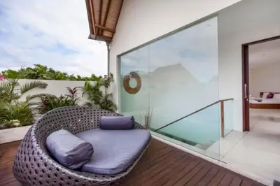 a wicker chair on a balcony with a glass wall at Ekavira Peaceful 2 BR Private Pool Villa in Seminyak