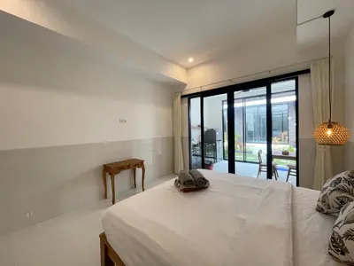 a bedroom with a white bed and a large window at Gede Awan Guesthouse in Kerobokan