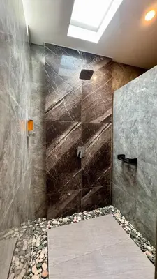 a bathroom with a shower with a stone wall at Villa Harmaka in Kerobokan