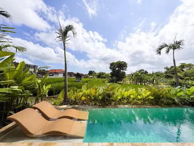 a resort pool with a chair and palm trees at Desa Hut - Serene Tropical Hideaway Rice Fields near Seminyak in Kerobokan