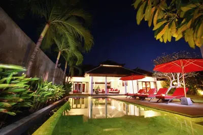 a pool with chairs and umbrellas next to a house at Villa Alma in Legian