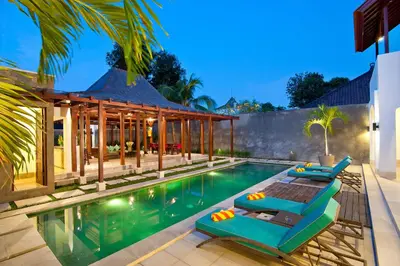 an infinity pool with two lounge chairs and a house at Villa Amalia Walk To Legian Beach in Legian