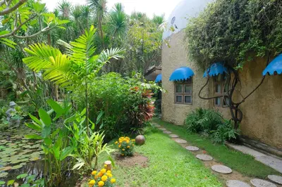 a garden with plants and a building with blue umbrellas at Mosaic Villa Sanur in Sanur
