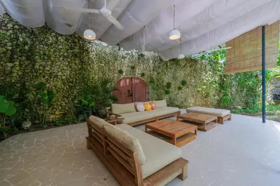 a patio with couches and tables and a green wall at Mosaic Villa Sanur in Sanur