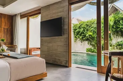 a bedroom with a tv on a wall next to a pool at Charity Stunning Grand 1 BR Pool Villa With Jacuzzi in Seminyak