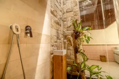 a bathroom with a stone wall and a plant at Emica Peaceful Royal 1 BR Pool Villa With Bathtub in Legian