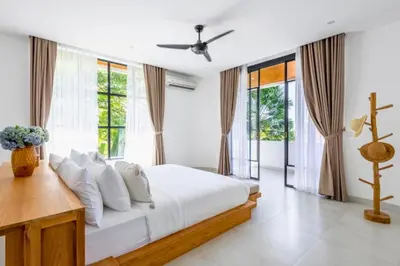 a bedroom with a bed with white sheets and windows at Ashlyn Elegant 4 BR Private Pool Villa in Canggu