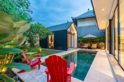 a home with a swimming pool and red chairs next to a house at Villa Semilir Pagi, Canggu in Canggu