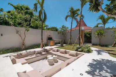 a patio with a couch in a backyard with palm trees at Villa Batu, Superb 4BR beachside in Canggu