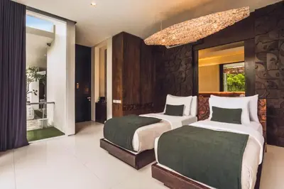 two beds in a bedroom with a stone wall at Varenya Cozy 1 BR Suite Twin Room in Kerobokan