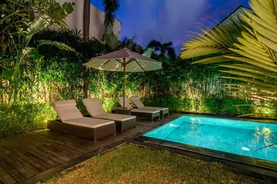 a pool with lounge chairs and an umbrella next to a pool at Villa Rajawali 3BR Private Villa Near Beach in Canggu