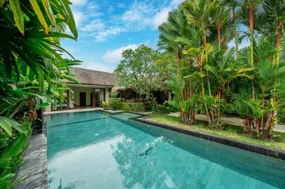 a swimming pool in front of a house with palm trees at Villa Rajawali 3BR Private Villa Near Beach in Canggu