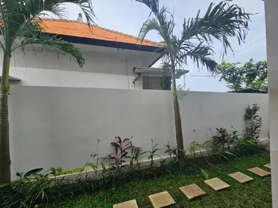 a white fence in front of a house with palm trees at Kubu Semangka in Sanur