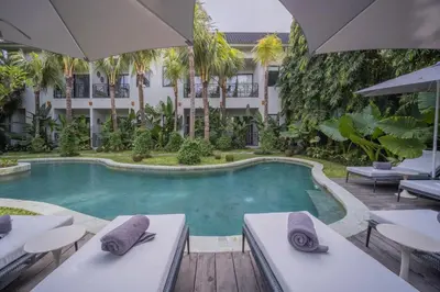 a swimming pool with tables and umbrellas in front of a building at Anam Mani New Room Central Seminyak in Seminyak