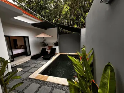 a patio with a pool with chairs and an umbrella at BEN & B Villa 2 in Kerobokan