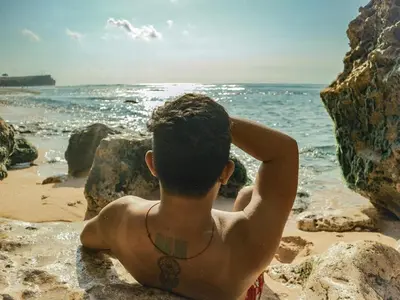 a young man sitting on the beach looking at the ocean at 3BR Canggu Batu Belig Tropicana Villa - Walk to Beach in Canggu