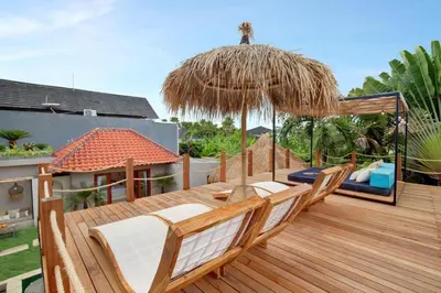 a wooden deck with chairs and an umbrella at 5BR Luxury Berawa Canggu with Butler in Canggu