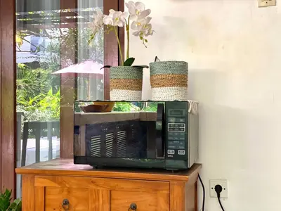 a microwave sitting on top of a wooden cabinet with flowers at Superb Location! Modern 2BR Seminyak Oasis with Pool & Garden in Seminyak