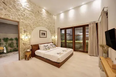 a bedroom with a bed and a tv and a stone wall at 6BR Seminyak Oasis with 2 Private Pools in Seminyak